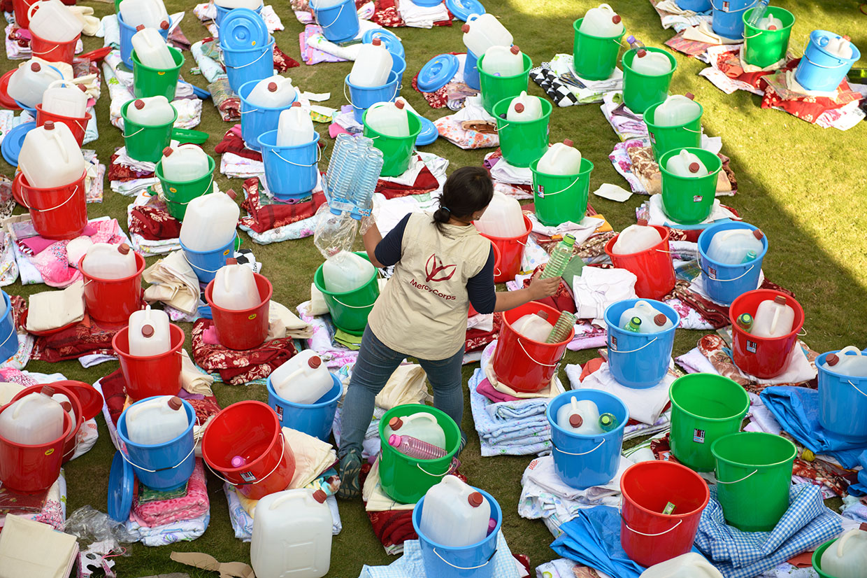 A mercy corps team member standing among buckets filled with emergency supplies in nepal