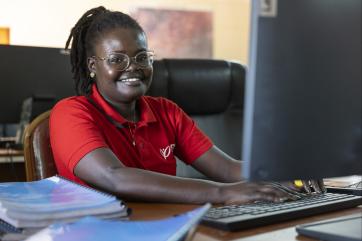 Kenyan woman smiling while seated in front of computer in office space.