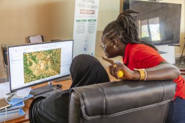 Two kenyan women work in front of a computer together on a mapping program.