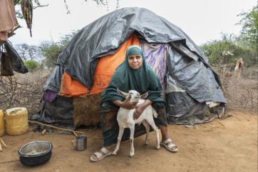 Kenyan woman with goat in front of tent.