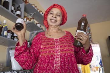 Senegalese female entrepreneur stands in her business smiling and holding her products.