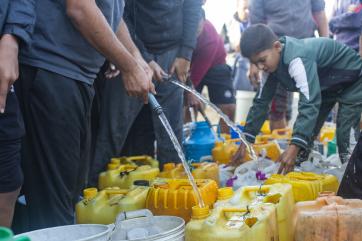 Palestinian boy collecting water amidst others doing the same.