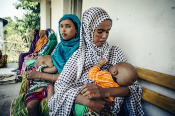 Amina holding her son, emran. she is seated next to another woman who is also holding an infant.