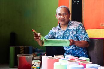 Indonesian man smiling holding paint brush working in studio.