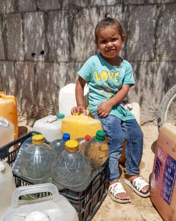 Young palestinian child sits atop filled jerrycans.