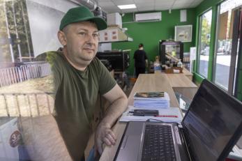 Ukrainian man stands at desk with laptop open.
