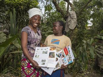 Two women pictured smiling, holding papers