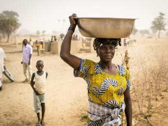 Woman carrying a large container balanced on her head, supported by her hand