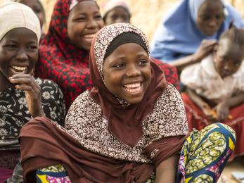 A girl sitting on the ground with other girls nearby, all laughing, in nigeria